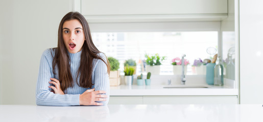 Wide angle picture of beautiful young woman sitting on white table at home afraid and shocked with...