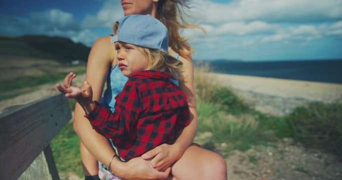 Little toddler sitting on bench at the beach with is mother