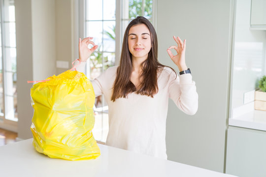 Beautiful young woman taking out the garbage from the rubbish container relax and smiling with eyes closed doing meditation gesture with fingers. Yoga concept.