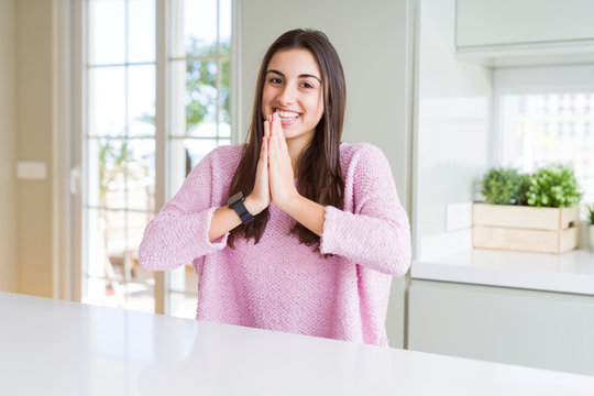 Beautiful young woman wearing pink sweater praying with hands together asking for forgiveness smiling confident.