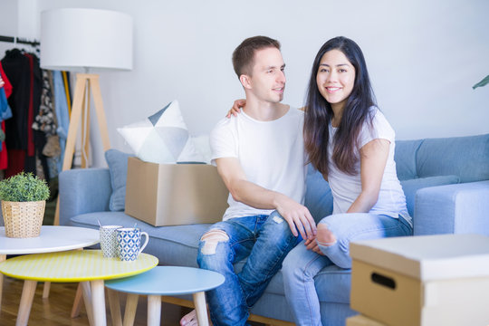 Young beautiful couple sitting on the sofa drinking coffee at new home around cardboard boxes