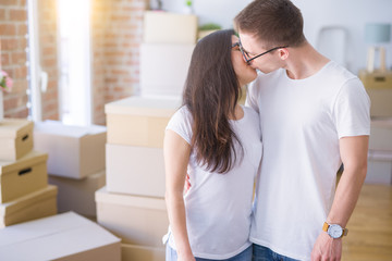 Young beautiful couple kissing wearing glasses standing at new home around cardboard boxes