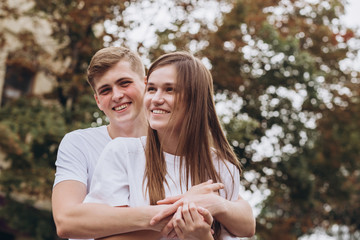 Happy young couple walks the streets of the city and hold hands. guy and girl in white t-shirts and jeans outdoors. Teenagers cuddling against the backdrop of an autumn tree. Couple close-up portrait