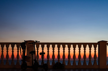 Two with a backpack and a women's bag tourists left near the fence with balusters against the sunset by the sea.