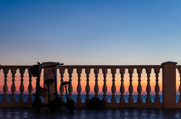 Two with a backpack and a women's bag tourists left near the fence with balusters against the sunset by the sea.