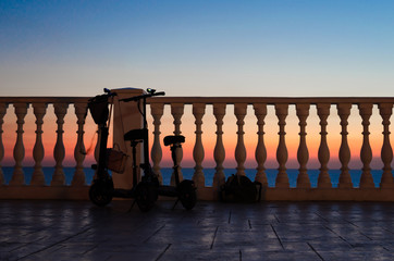 Two with a backpack and a women's bag tourists left near the fence with balusters against the sunset by the sea.