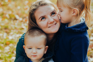Fototapeta premium Beautiful young mother with daughter and son are walking in the autumn park. close-up portrait