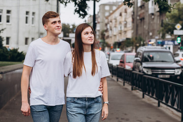 young couple walks the streets of the city and hold hands. guy and girl in white t-shirts and jeans outdoors. Teenagers walk in the autumn city. Happy young couple.