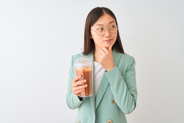 Young chinese woman drinking tomato smoothie over isolated white background serious face thinking...