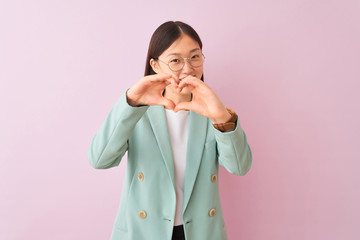 Young chinese businesswoman wearing jacket and glasses over isolated pink background smiling in love showing heart symbol and shape with hands. Romantic concept.