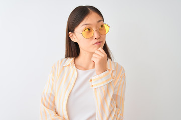 Young chinese woman wearing striped shirt and glasses over isolated white background serious face...