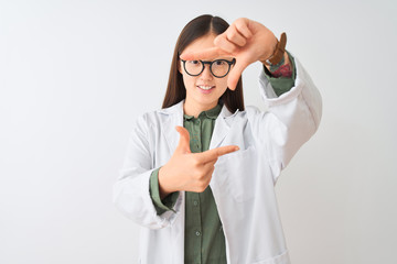 Naklejka premium Young chinese scientist woman wearing coat and glasses over isolated white background smiling making frame with hands and fingers with happy face. Creativity and photography concept.