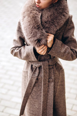 girl in a warm coat outdoors. model in outerwear. brunette in a long beige coat with fur walks...