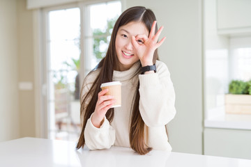 Beautiful Asian woman drinking a coffee in a take away paper cup with happy face smiling doing ok sign with hand on eye looking through fingers