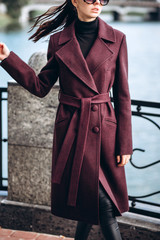 girl in a warm coat outdoors. model in outerwear. A brunette in a long burgundy coat walks along the embankment of the river. beautiful girl in a fashionable casual coat. spring autumn collection.