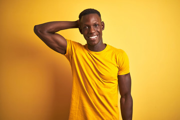 Young african american man wearing casual t-shirt standing over isolated yellow background smiling confident touching hair with hand up gesture, posing attractive and fashionable