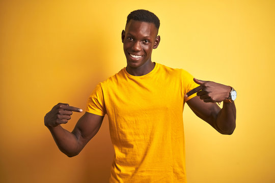 Young african american man wearing casual t-shirt standing over isolated yellow background looking confident with smile on face, pointing oneself with fingers proud and happy.