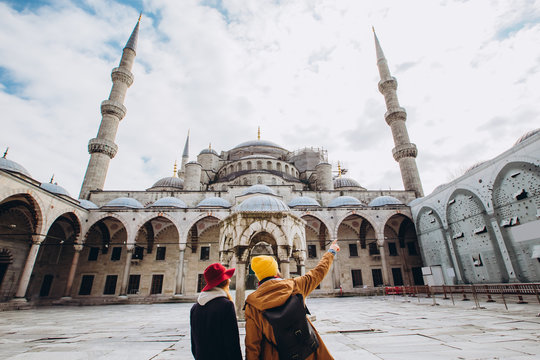 A young European couple walks in the courtyard of the Blue Mosque in Istanbul, Turkey. Traveler guy and girl in yellow hats walk in winter Istanbul. cloudy autumn day in Istanbul.
