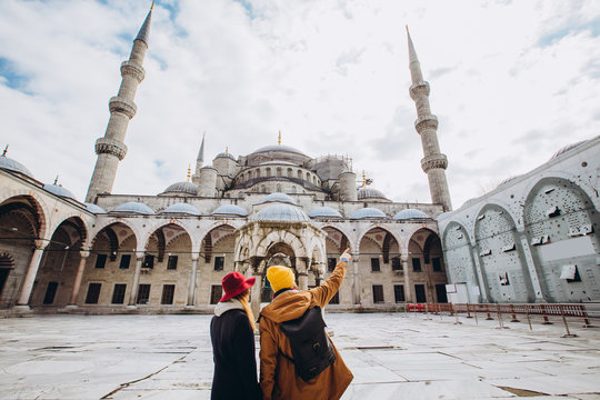 A young European couple walks in the courtyard of the Blue Mosque in Istanbul, Turkey. Traveler guy and girl in yellow hats walk in winter Istanbul. cloudy autumn day in Istanbul.
