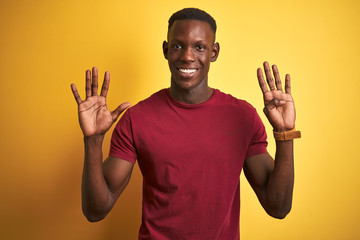 Young african american man wearing red t-shirt standing over isolated yellow background showing and pointing up with fingers number nine while smiling confident and happy.