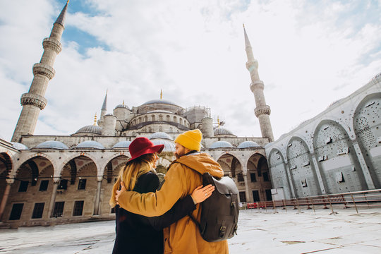 A young European couple walks in the courtyard of the Blue Mosque in Istanbul, Turkey. Traveler guy and girl in yellow hats walk in winter Istanbul. cloudy autumn day in Istanbul.