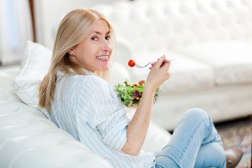 Mature woman eating a healthy salad on her sofa