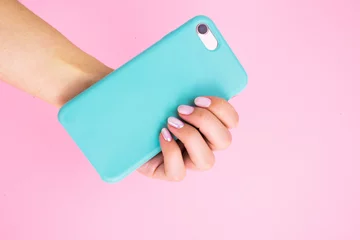 Smartphone in a mint case in hand with manicure on a pink background. © Ekaterina Pichukova