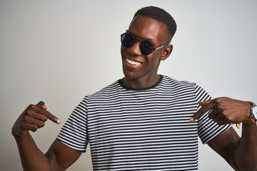 Naklejka premium African american man wearing striped t-shirt and sunglasses over isolated white background looking confident with smile on face, pointing oneself with fingers proud and happy.
