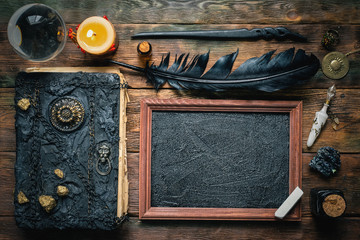 Blackboard with a copy space, crystal ball, magic book and magical wand on the wooden table background. School of magic concept.