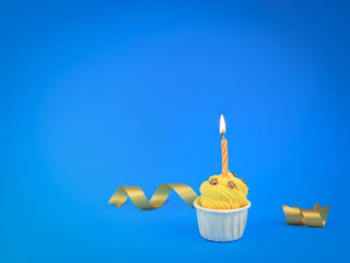 Sweet bright yellow cupcake with bow candle on blue background with copy space. Happy birthday party