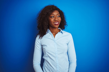 Obraz premium African american businesswoman wearing shirt standing over isolated blue background looking away to side with smile on face, natural expression. Laughing confident.