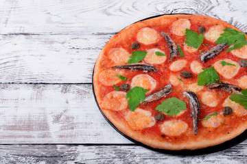 Round pizza with anchovies, capers, mozzarella cheese and tomato sauce garnished with fresh parsley on white table