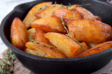 Golden roasted potato wedges in a cast iron pan on white wooden table