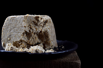 Big piece of sunflower and sesame halva on wooden table against black background. Eastern dessert