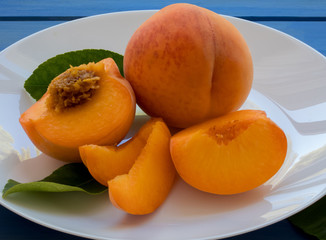 Naklejka na ściany i meble Yellow peaches full and cut on white plate, on blue table. Closeup, fruits