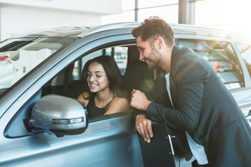 handsome man manager consulting young beautiful woman client while looking for new car in dealership center