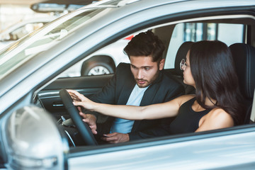 young couple handsome man and beautiful woman looking for new car in dealership center