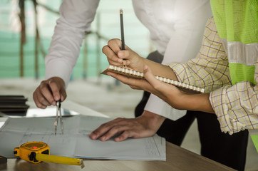 construction worker team writing and planning about building plan with blueprint, construction tools on conference table at construction site, contractor, business, industry and construction concept