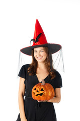 trick or treat. young caucasian woman smiling and holding orange pumpkin head dressed in black witch clothing costume and red hat on isolated white background, holiday and halloween festival concept