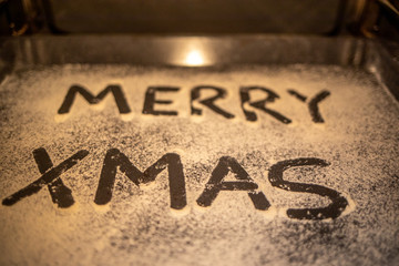 the words Merry Xmas is written on a baking tray sprinkled with powdered sugar or flour