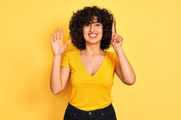 Young arab woman with curly hair wearing t-shirt standing over isolated yellow background showing and pointing up with fingers number six while smiling confident and happy.