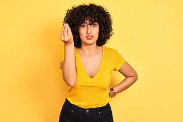 Young arab woman with curly hair wearing t-shirt standing over isolated yellow background Doing Italian gesture with hand and fingers confident expression