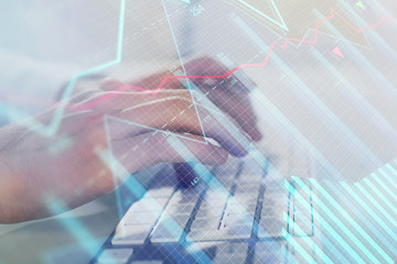 Double exposure of graph with man typing on computer in office on background. Concept of hard work. Closeup.