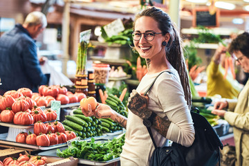 Happy smiling woman is carefully choosing fresh vegetables on a local farmer's market.