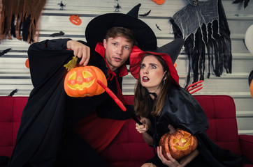 Halloween. couple young caucasian man and woman in vampires and witch clothing holding pumpkin head lantern and sitting on sofa in halloween party at home, holiday and halloween festival concept