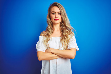 Young beautiful woman wearing white dress standing over blue isolated background skeptic and...