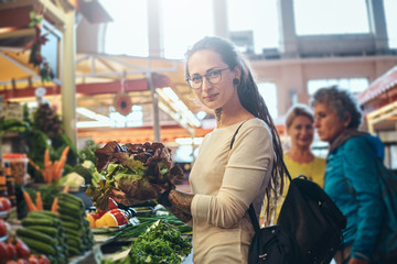 Young attractive woman with tattooes choosing fresh salad at vegetable market.