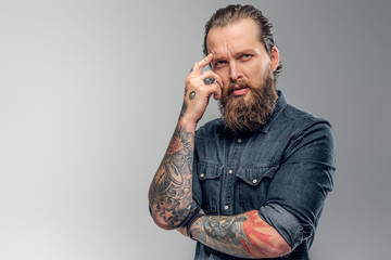 Tired tattooed man with beard is posing for photographer at photo studio.