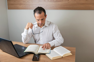 43 year old man biting the leg of his glasses and focused on his reading.