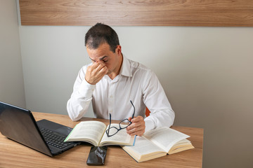 43 year old man holding his glasses and tired of reading books.